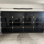 A black glass-paneled garage door in a clean, organized garage with concrete floor and some tools along the left wall.
