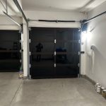 Clean, empty garage with closed glass doors, paint cans stacked in the corner, and bright overhead lighting.